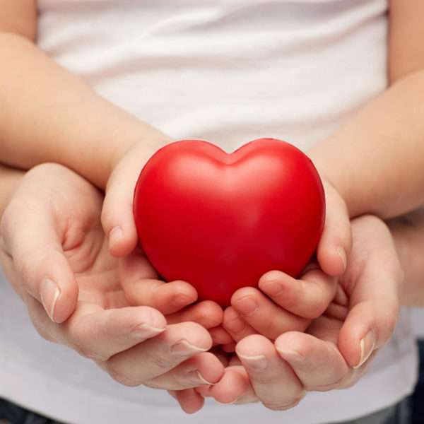 Mão de criança e de adulto segurando um coração como forma de ilustrar a doação de óvulos