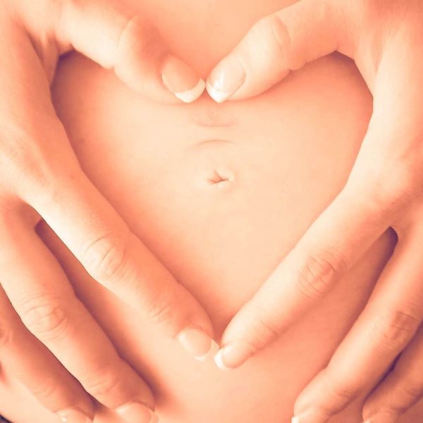 Mulher grávida fazendo coração com as mãos em volta do umbigo