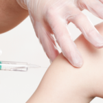 ombro e braço feminino tomando vacina com uma agulha sendo segura por mãos com luvas